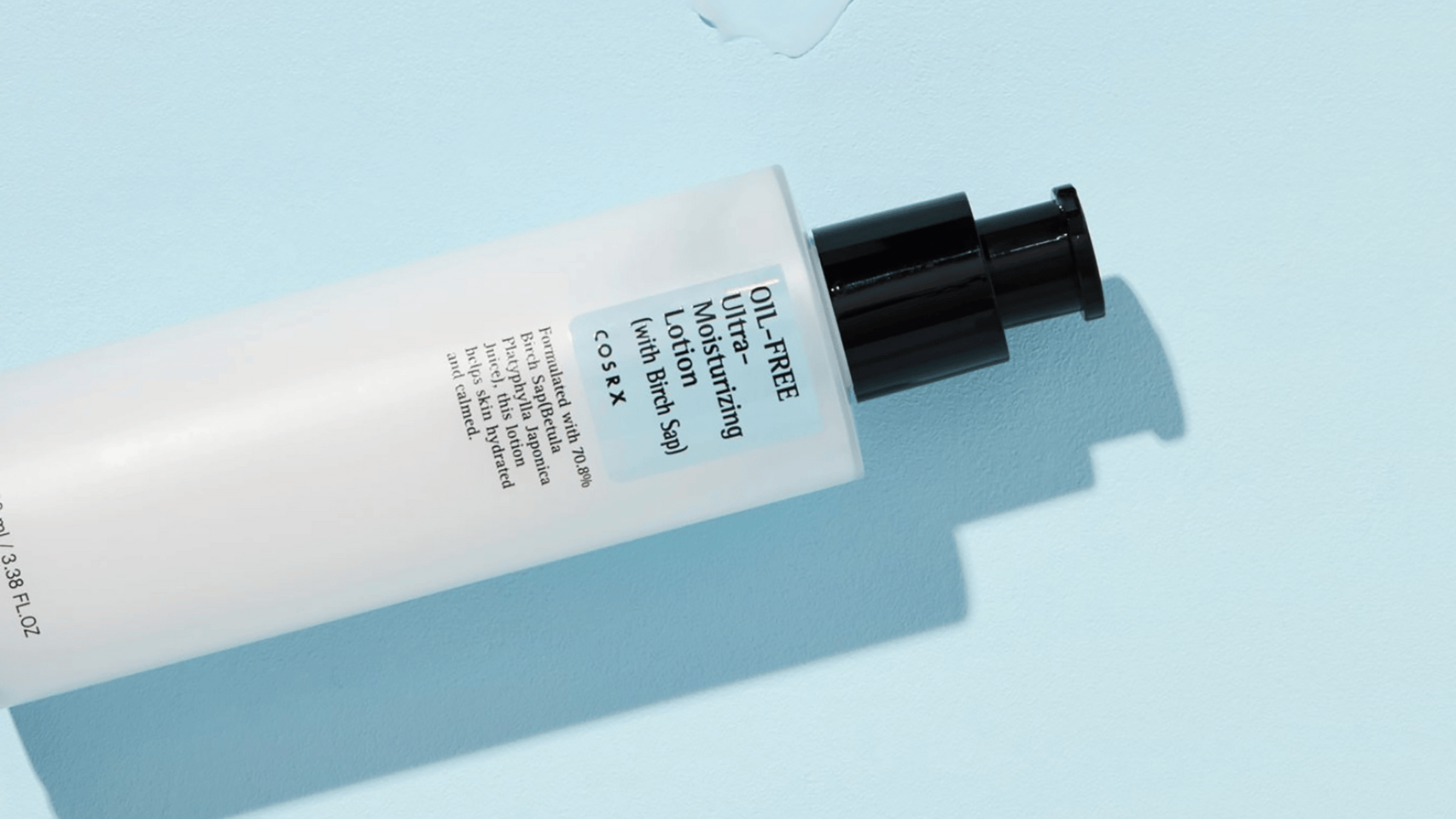 En liggande tub av COSRX Oil-Free Ultra-Moisturizing Lotion på en blå bakgrund med en skugga.