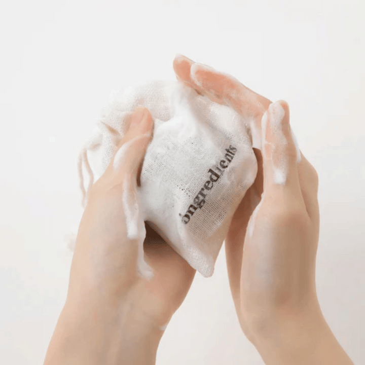 Händer som löddrar upp Óngredients Jeju Green Tea Cleansing Ball i tygpåse – vegansk ansiktsrengöring med grönt te.