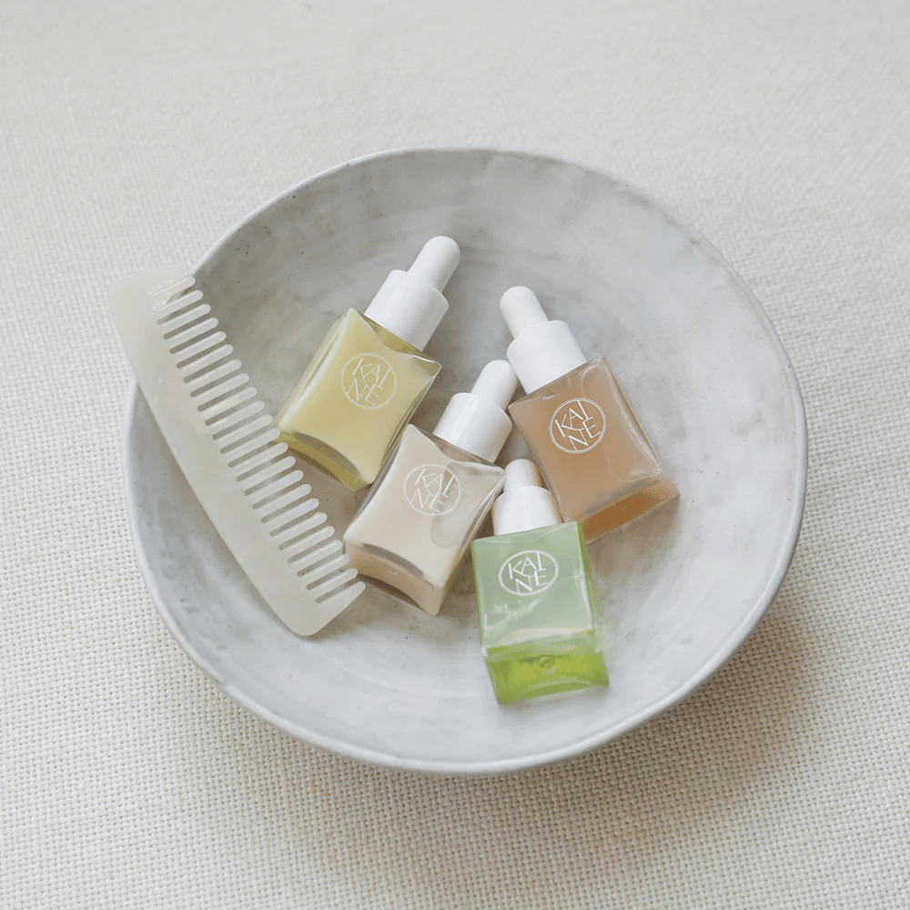 Fyra små serumflaskor från KAINÉ Serum Discovery Kit ligger i en vit skål bredvid en kam, med en naturlig och lugn bakgrund i beige ton.