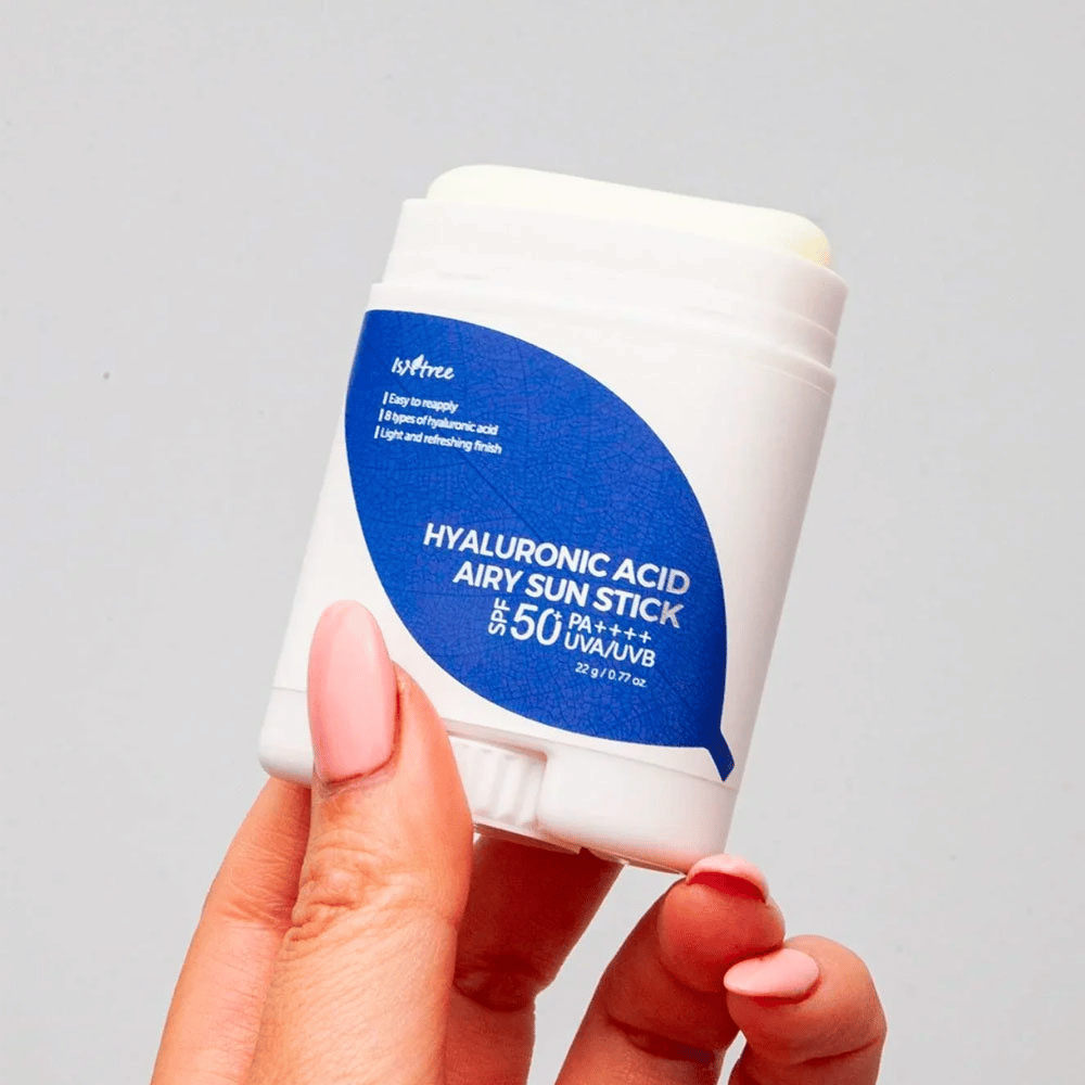 En hand håller i en vit solsticka med blå etikett från märket Isntree. Produkten heter "Hyaluronic Acid Airy Sun Stick" och har solskyddsfaktor SPF 50+ PA++++.