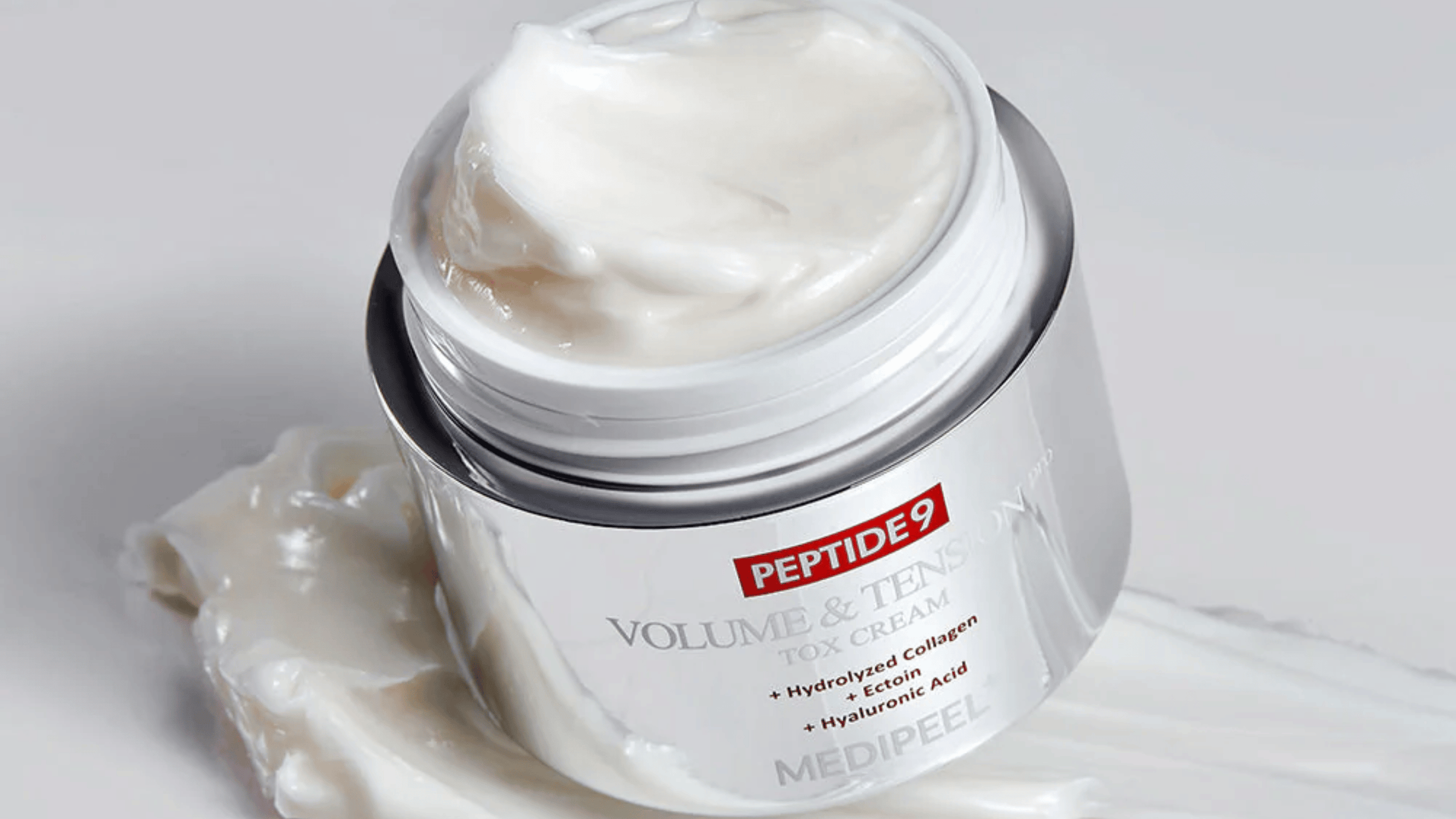 Närbild på MEDI-PEEL Peptide 9 Volume & Tension Tox Cream i silverburk. Den krämiga formulan innehåller hydrolyserat kollagen, ectoin och hyaluronsyra för fastare och återfuktad hud.