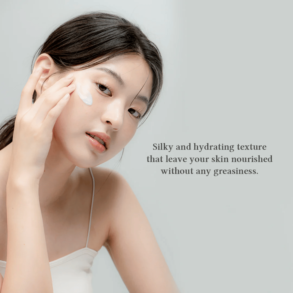 The image shows a woman applying a face cream. The text on the image describes the product as silky and moisturizing, emphasizing that it nourishes the skin without leaving an oily feeling. This suggests that the cream has a light and pleasant consistency that is well absorbed by the skin.
