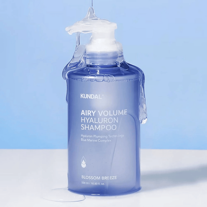 KUNDAL Airy Volume Hyaluron Shampoo Blossom Breeze i blå pumpflaska, med hyaluron och Blue Marine Complex, fotograferad med rinnande vatten.