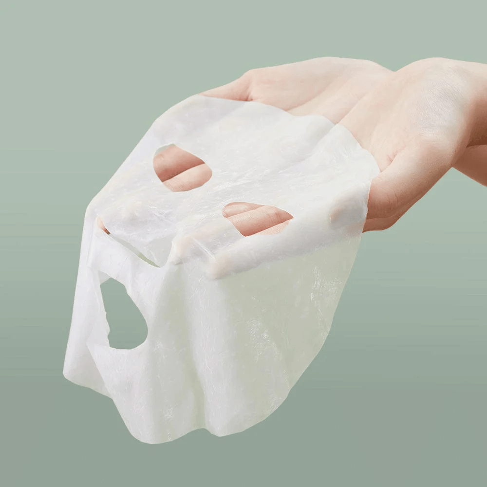 A person's hand holding Anua Heartleaf 77% Soothing Sheet Mask.