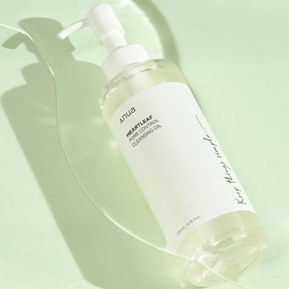 The image features ANUA Heartleaf Pore Control Cleansing Oil, a cleansing oil with a pump design. The bottle is transparent, and the contents appear to have a light, oily consistency. The label bears the brand's logo and product name in simple and elegant text, contributing to a sense of minimalist beauty and purity. It says "Keep things simple" as part of the design, suggesting a philosophy of simplicity in the skincare routine. The bottle contains 200 ml of product.