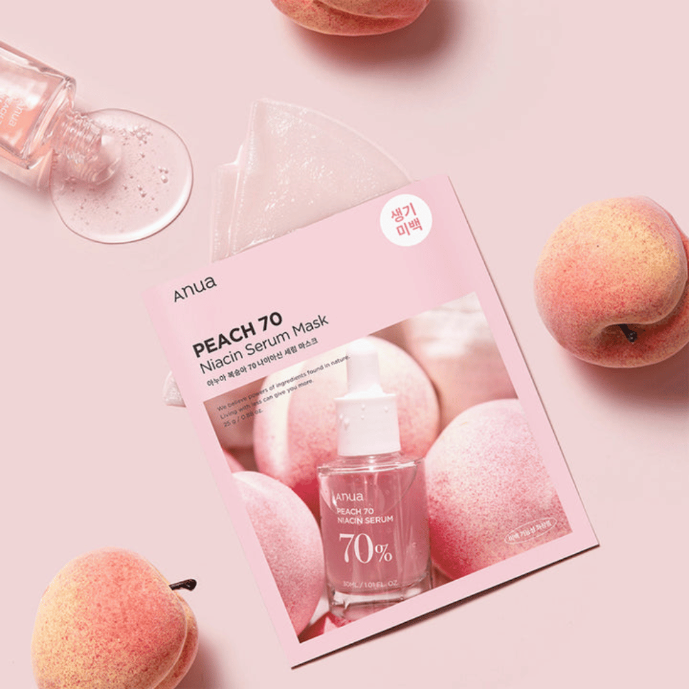 An image of Anua PEACH 70 Niacin Serum Mask, surrounded by peaches and a bottle of serum. The image has a soft pink background, which complements the pink packaging and highlights the product and ingredients.