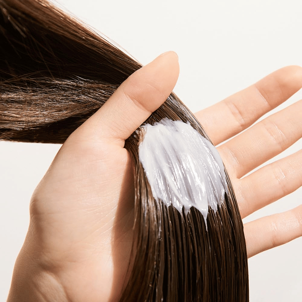 Hand applies Nature Republic Argan Essential Moisture Repairing Hair Mask in wet hair – moisturizing mask that strengthens and softens the hair.