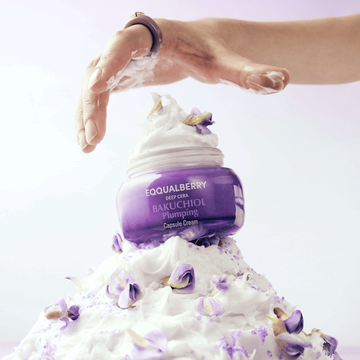 EQQUALBERRY Bakuchiol Plumping Capsule Cream placerad ovanpå en hög av vispad kräm med blomblad – symboliserar fukt och vård.