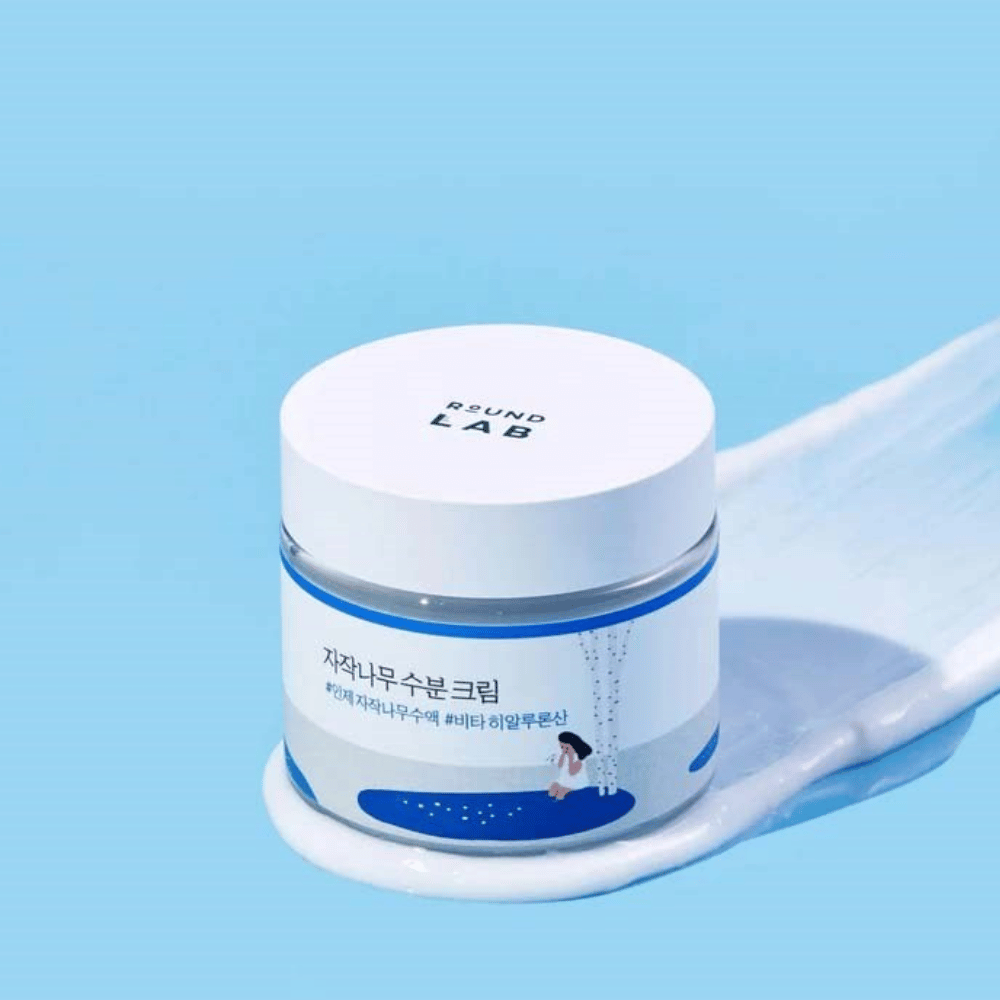 Round Lab Birch Juice Moisturizing Cream in a blue-tinted jar with a white lid, standing in a layer of cream against a blue background.