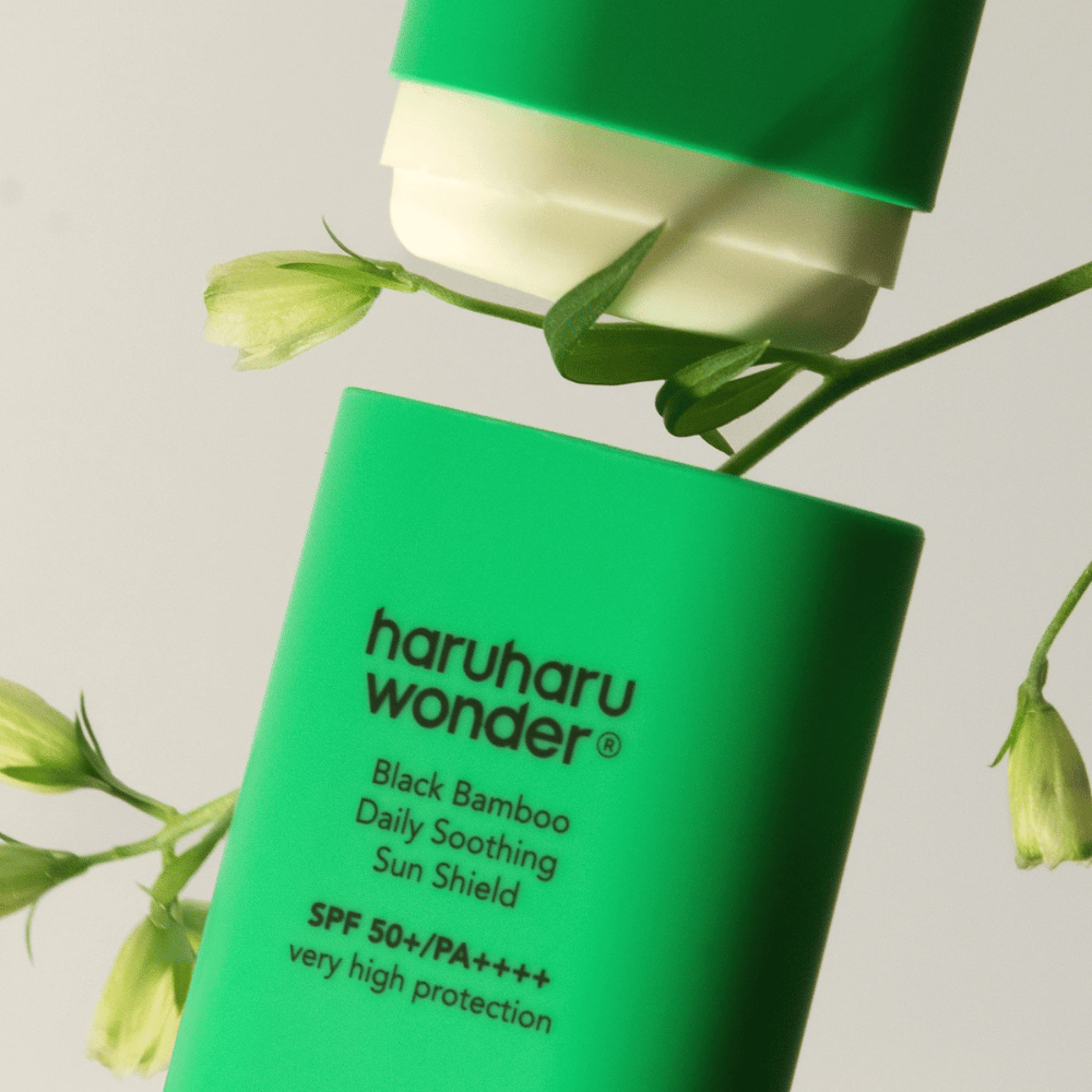 Close-up of Haruharu Wonder Black Bamboo Daily Soothing Sun Shield – a green stick format sunscreen with SPF 50+ PA++++, surrounded by green plant details.