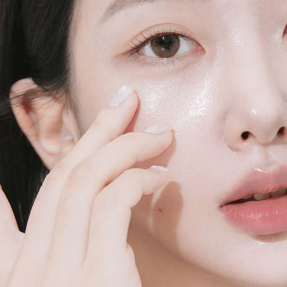 Close-up of a woman applying eye cream under the eye with her fingertips. The skin looks hydrated, shiny, and cared for with a natural glow.