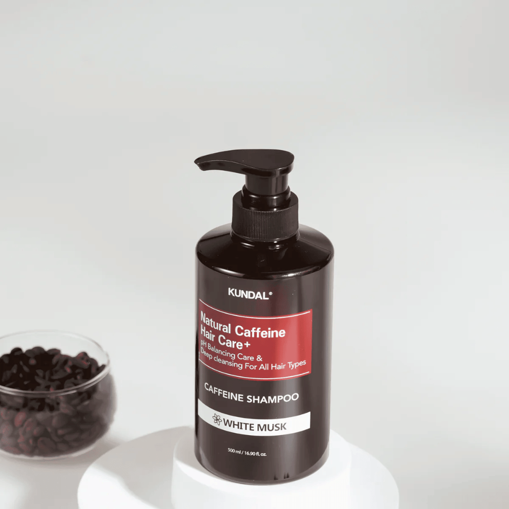 KUNDAL Natural Caffeine Hair Care+ Shampoo White Musk in a black pump bottle, 500 ml, placed next to a bowl of coffee beans.