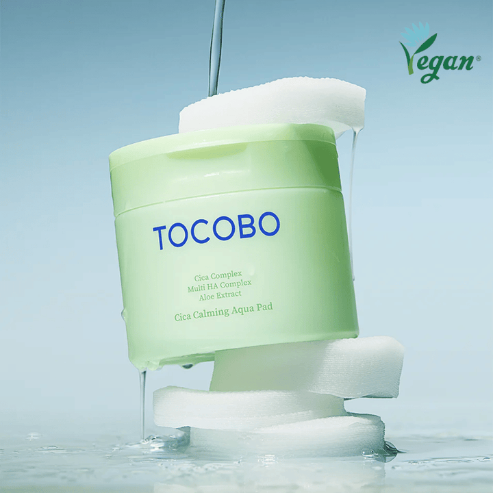 TOCOBO Cica Calming Aqua Pad placed among toner pads with flowing essence. The vegan symbol emphasizes the product's vegan formulation and skin-friendly profile.