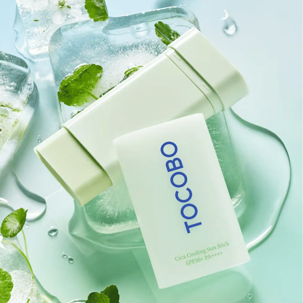 Tocobo Cica Cooling Sun Stick SPF50+ PA++++ on ice cubes with green plant leaves, conveying a cooling and refreshing feeling.
