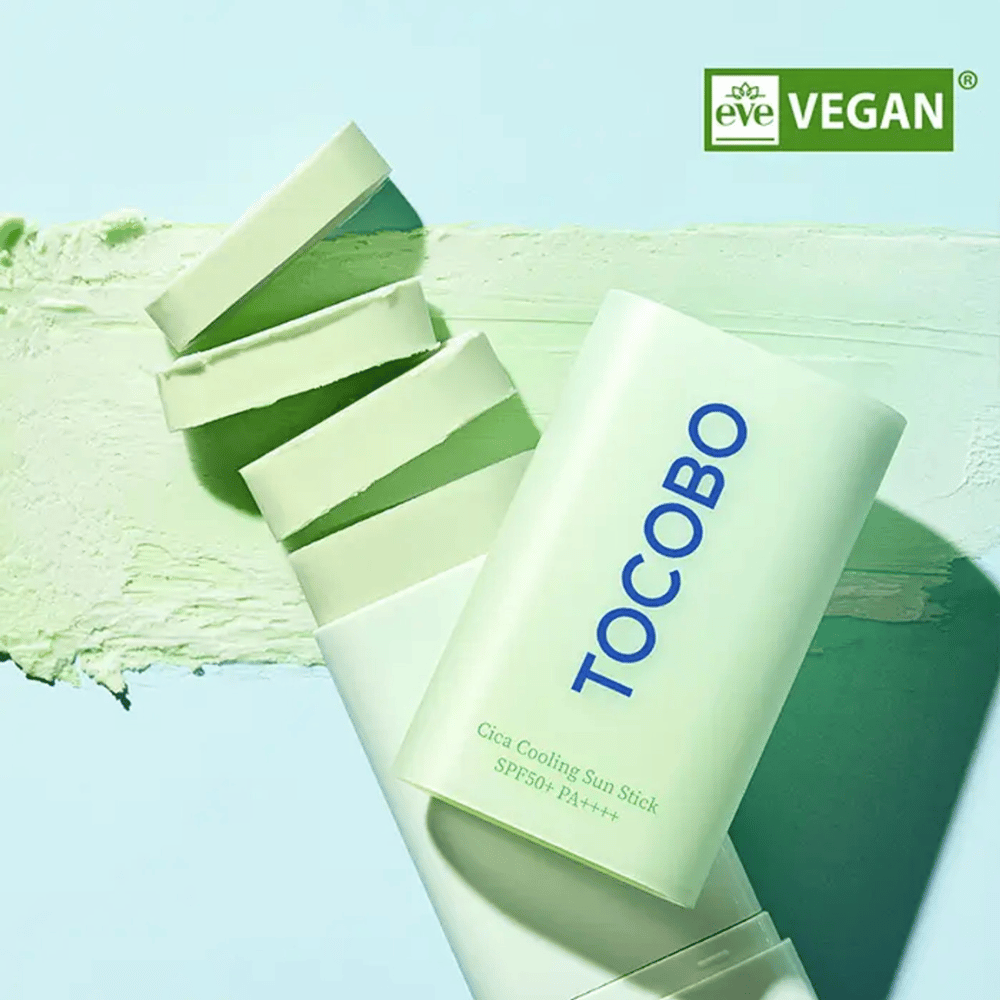 Tocobo Cica Cooling Sun Stick SPF50+ PA++++ in light green packaging with vegan labeling (EVE VEGAN), lying on a layer of green sun stick.