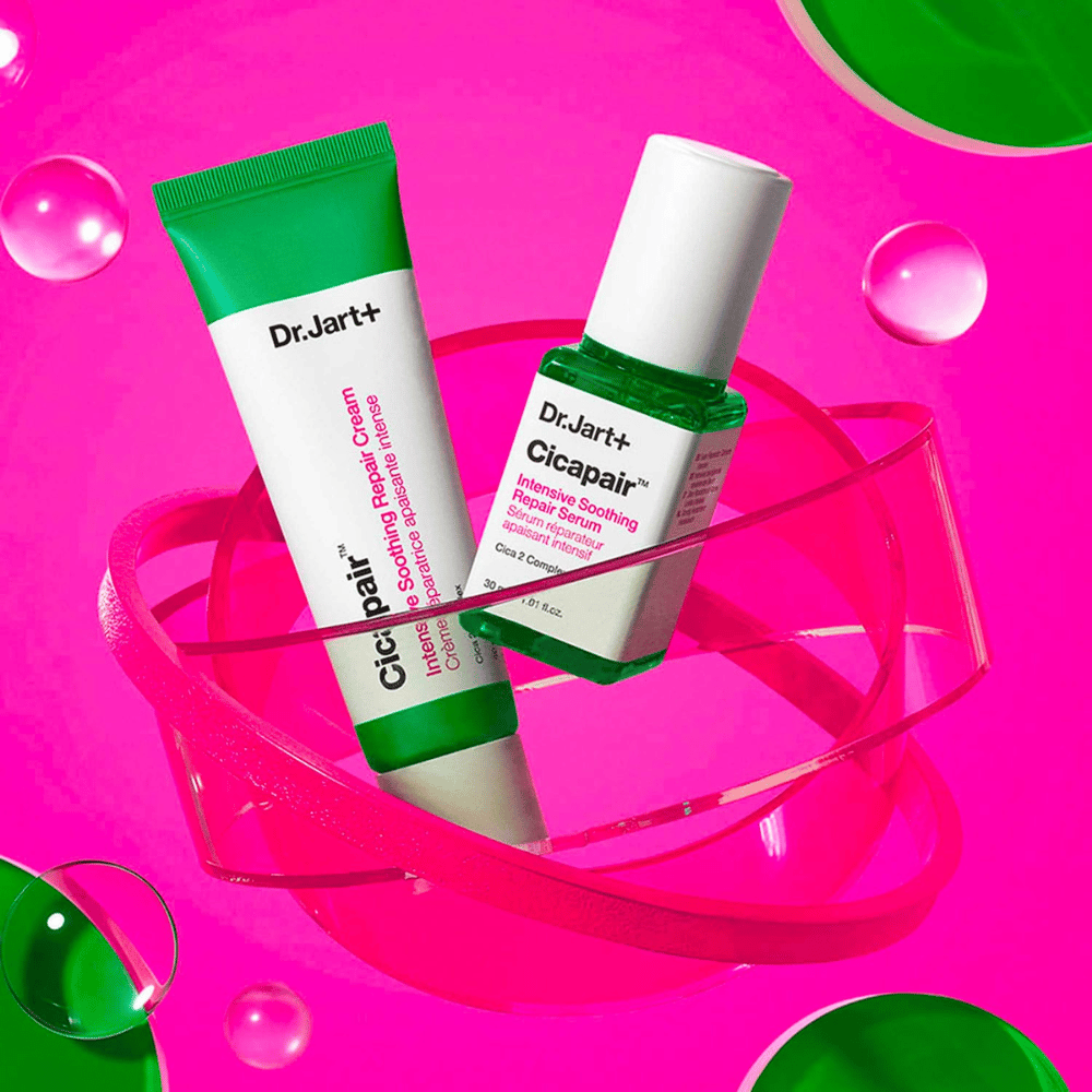 Dr.Jart+ Cicapair Intensive Soothing Repair Cream och Serum i gröna förpackningar, som står på en rosa cirkulär bas. Produkterna är framtagna för att lugna och reparera irriterad hud.