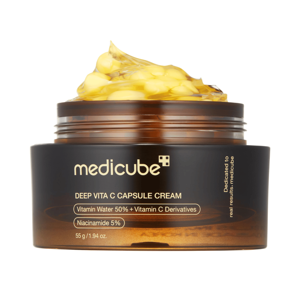 A close-up of "Medicube Deep Vita C Capsule Cream," showing the cream's consistency and the vitamin C capsules. The packaging is dark brown with gold text and describes the content of vitamin water (50%) and niacinamide (5%), providing a visual presentation of the product's moisturizing and skin-enhancing properties.