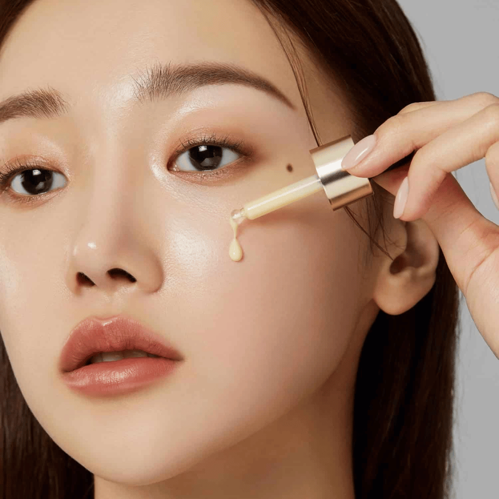Close-up of a woman applying Medicube Deep Vita C Ampoule with a gold-colored dropper. A drop of the serum is about to reach her skin, which has a natural glow. Perfect for giving a brighter and more even skin tone.
