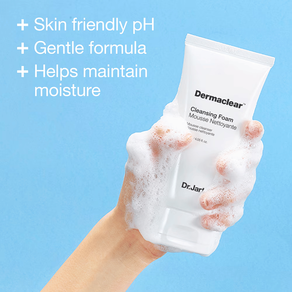 Hand covered in lather holding Dr.Jart+ Dermaclear Cleansing Foam against a blue background, with text highlighting skin-friendly pH, mild formula, and moisturizing properties.