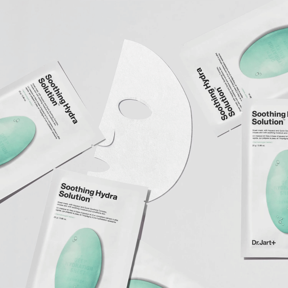 Several packages of "Soothing Hydra Solution" face masks from Dr.Jart+ are spread out on a light surface. An unfolded mask is placed in the middle, showing its white and perforated structure.