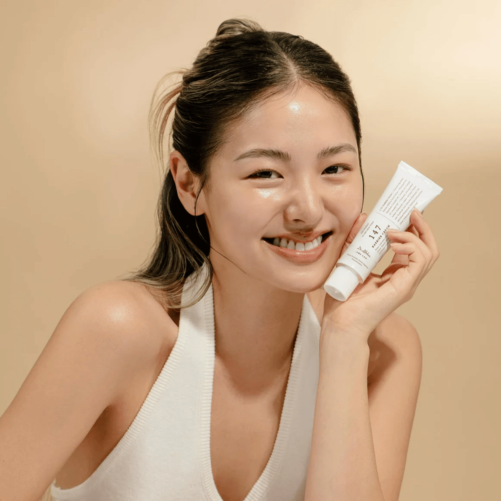 Model with glowing skin smiling and holding Dr. Althea 147 Barrier Cream – a Korean face cream for skin barrier and hydration.