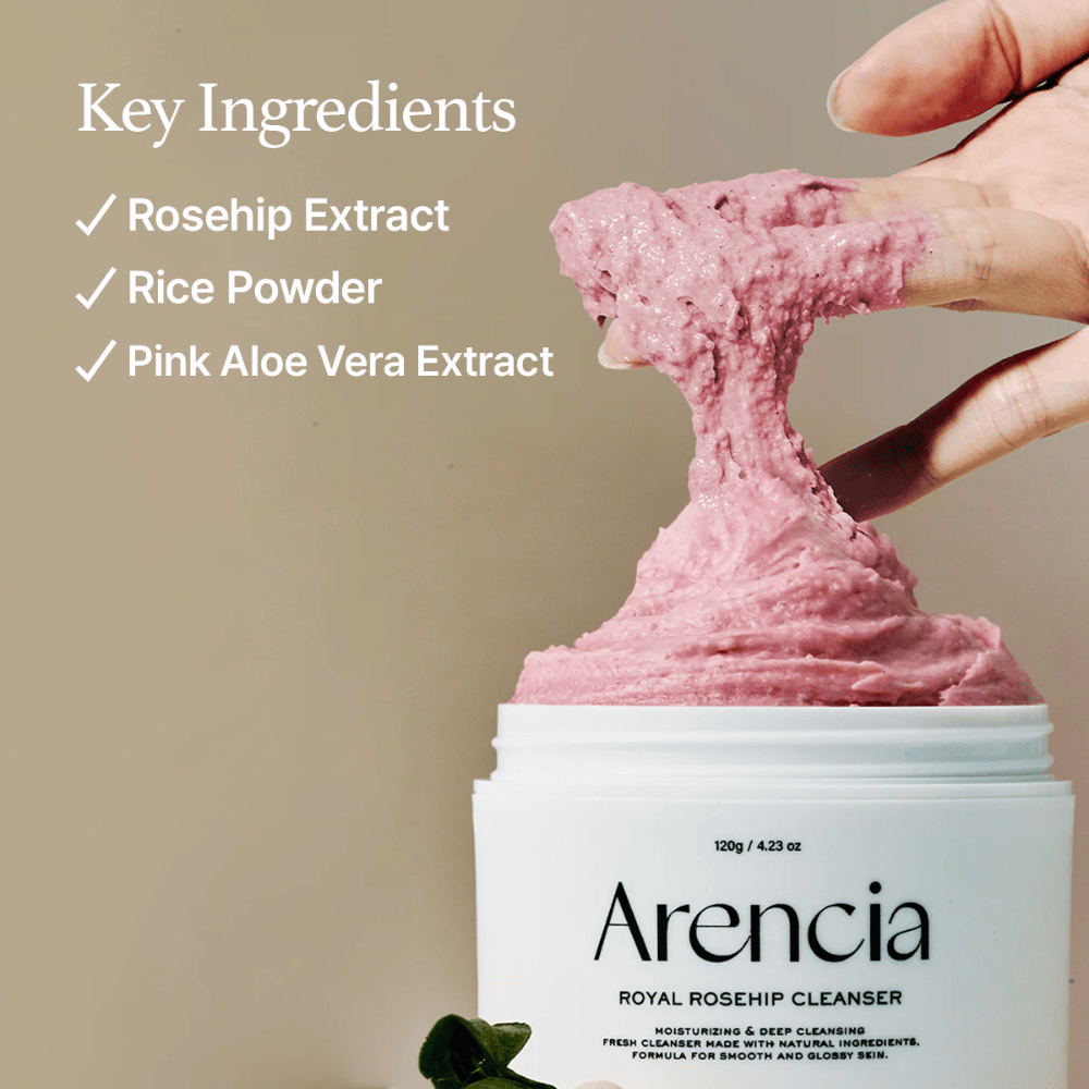 A hand lifts up the pink, fluffy cleansing texture from the jar Arencia Royal Rosehip Cleanser, with an ingredient list to the left: rosehip extract, rice powder, and pink aloe vera extract.
