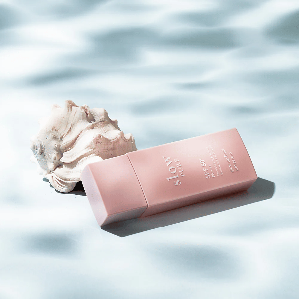 Slow Pure Glow Up Fluid Sun Serum by seashell and water effect, highlights sun protection and radiance.