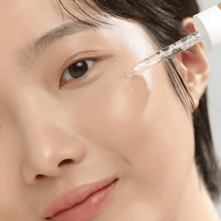 Närbild på kvinna som applicerar serum på kinden med pipett – hudvård som ger glow och återfuktning.