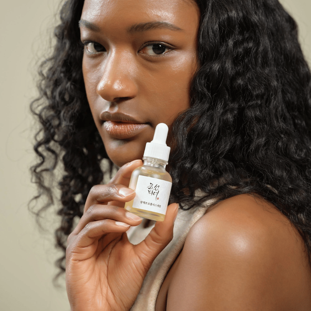 Woman with curly hair holding up a bottle of Beauty of Joseon Glow Serum with pipette, a moisturizing and radiance-giving skincare product.