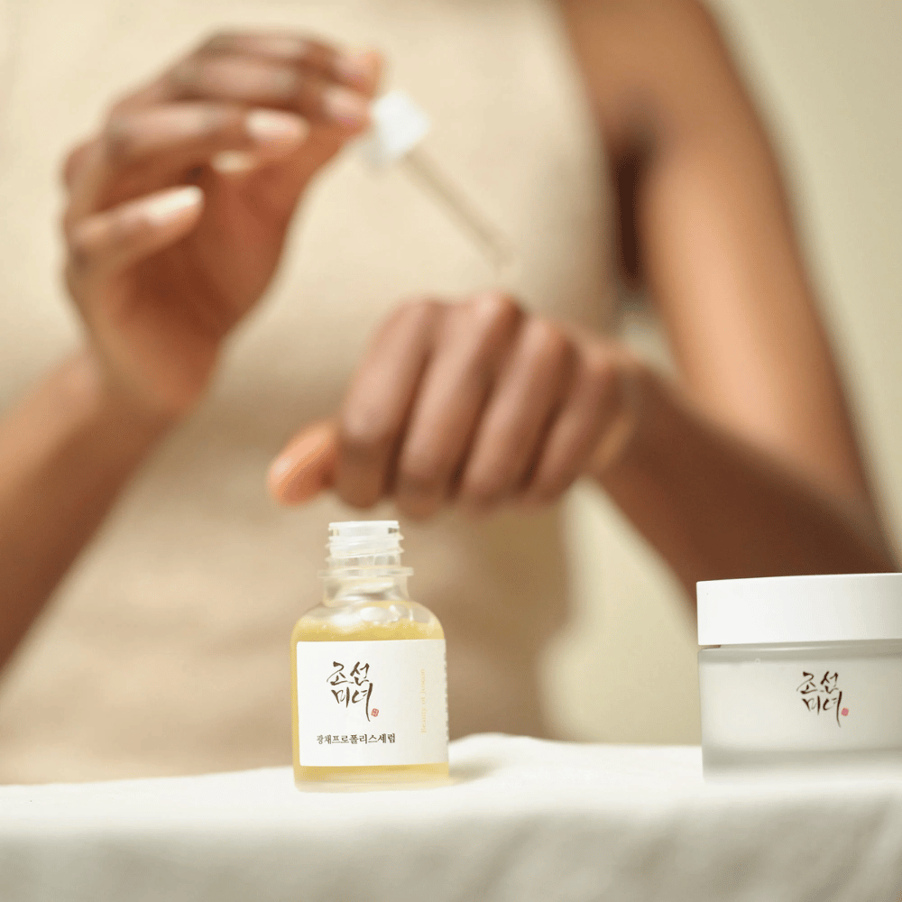 Person applying Beauty of Joseon Glow Serum with pipette from glass bottle, with a jar of the same series next to it on the table.