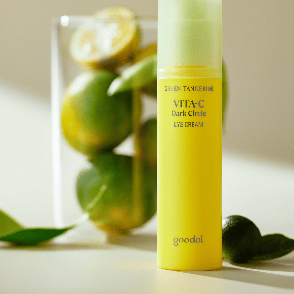 A bottle of Goodal Green Tangerine Vita C Dark Circle Eye Cream 30ml on a table next to a lime.