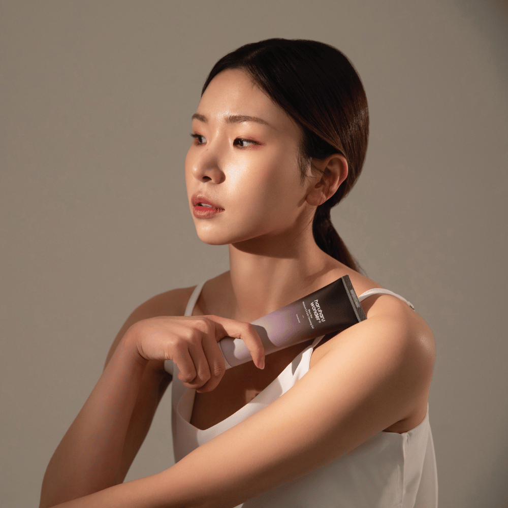 A young Asian woman holding a brush in her hand while using Haruharu Wonders Black Rice Moisture 5.5 Soft Cleansing Gel 100ml.