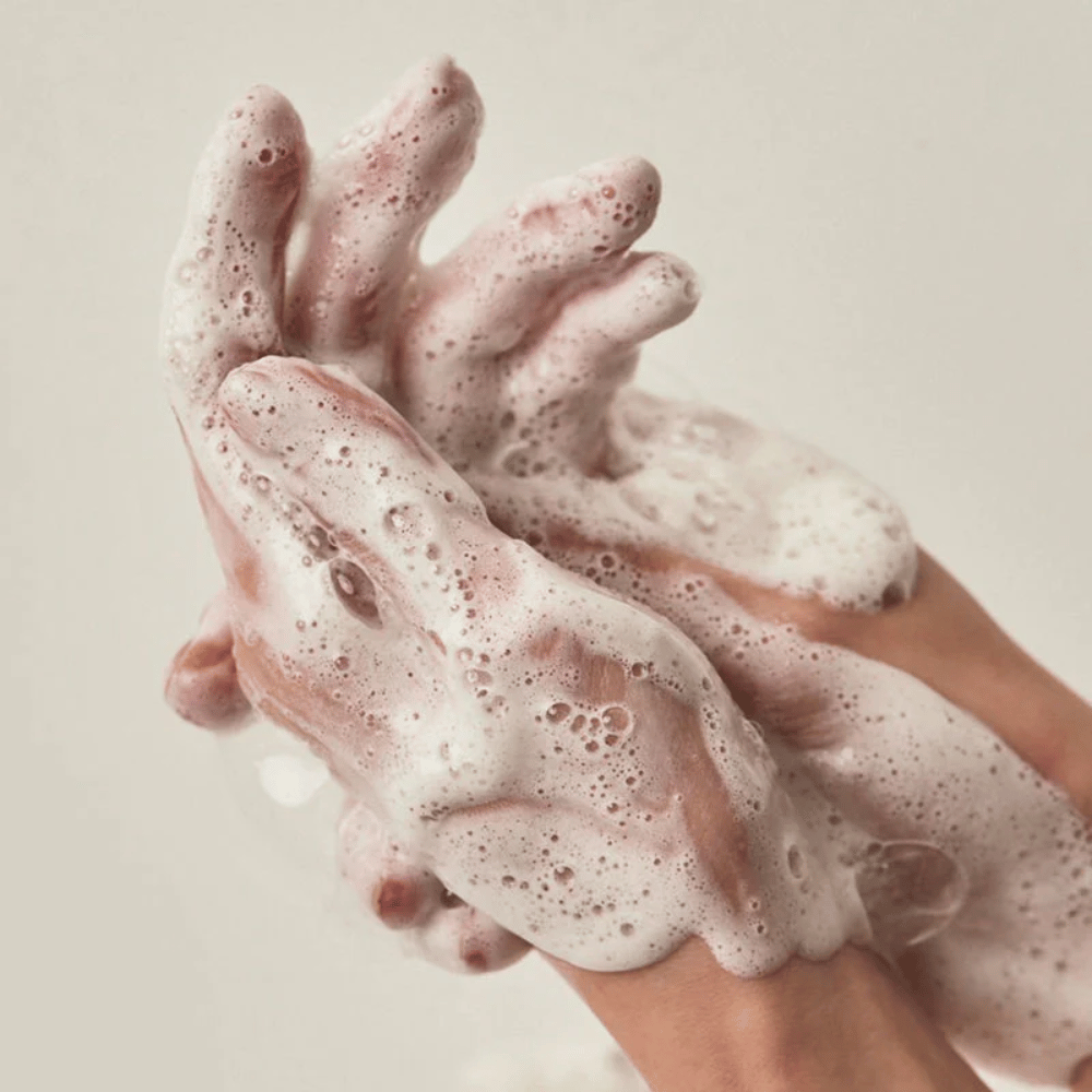 Close-up of hands covered in a rich and creamy cleansing foam. The image illustrates the product's lather and cleansing properties and provides a clear sense of use and texture.