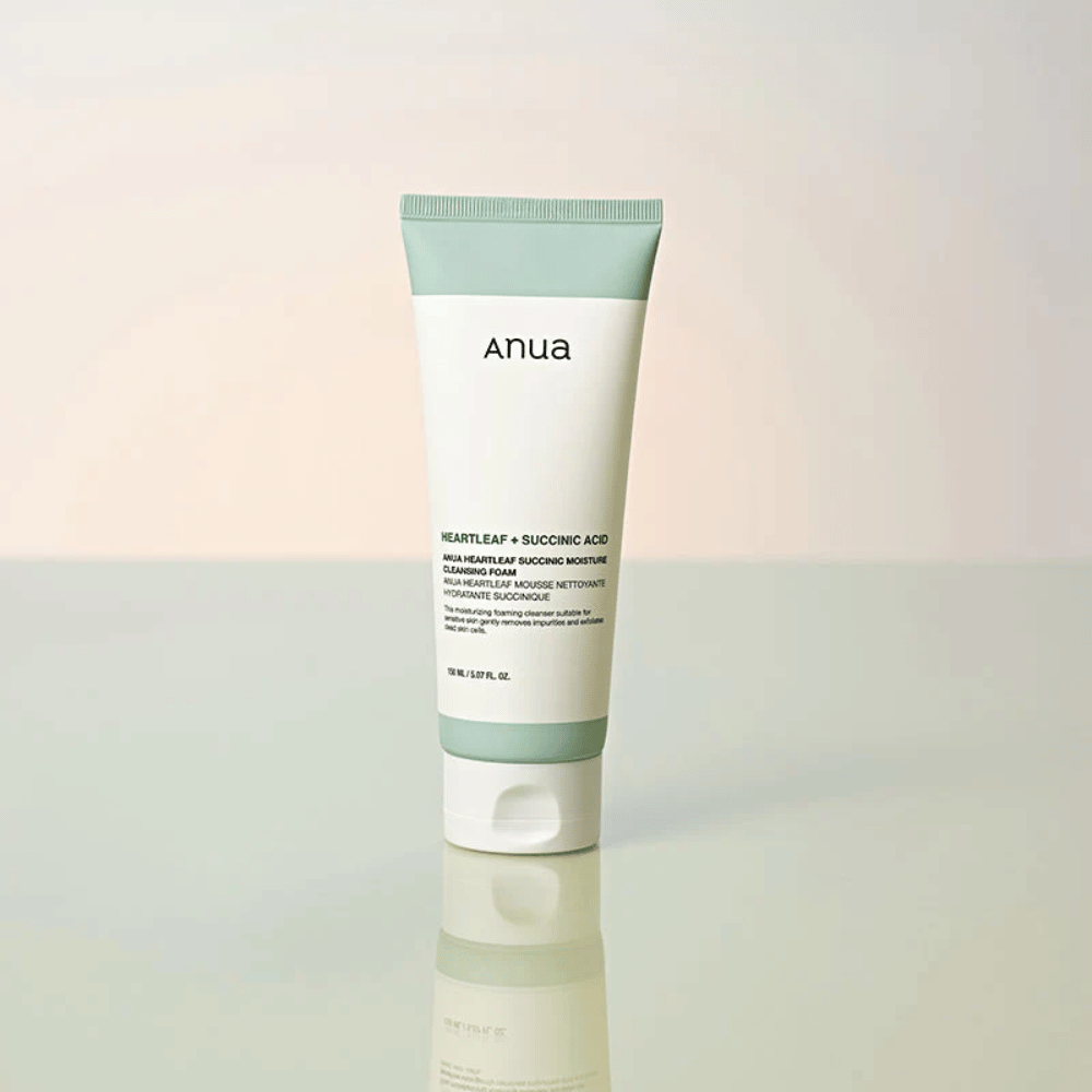Standalone product image of Anua Heartleaf + Succinic Acid Moisture Cleansing Foam. The product is shown standing on a reflective surface that clearly highlights the packaging design and the brand's sleek aesthetic.