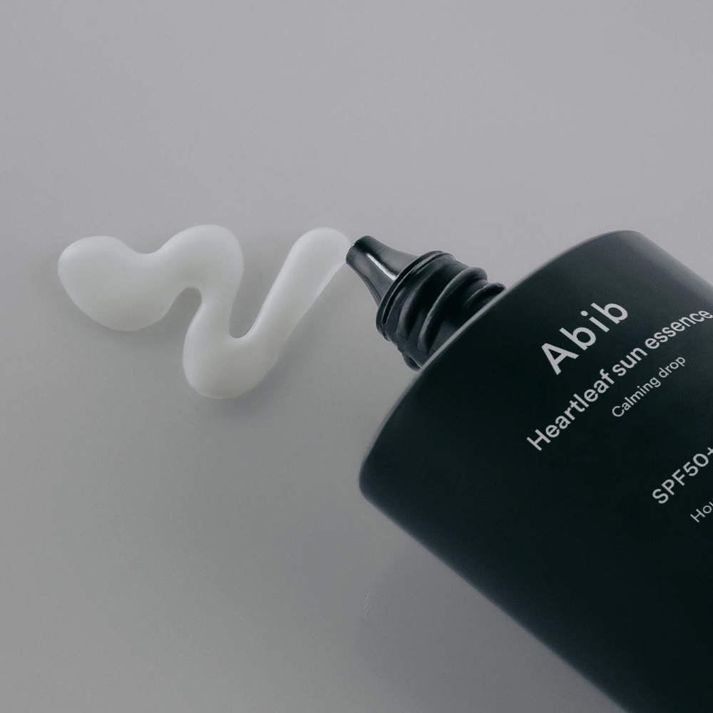 Close-up of Abib Heartleaf Sun Essence Calming Drop with the sunscreen squeezed out in a white, wavy line on a light surface.