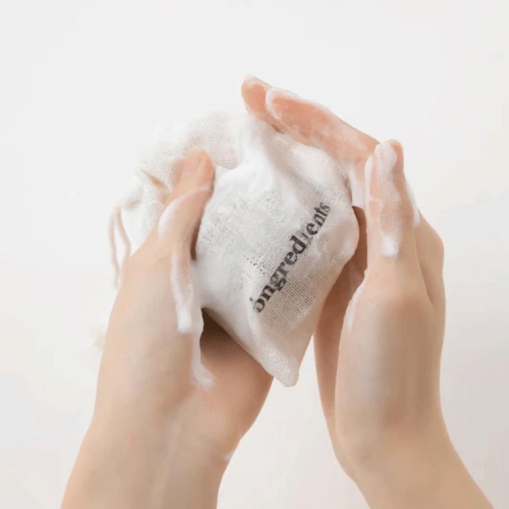 Hands lathering up Óngredients Jeju Green Tea Cleansing Ball in a fabric bag – vegan facial cleanser with green tea.