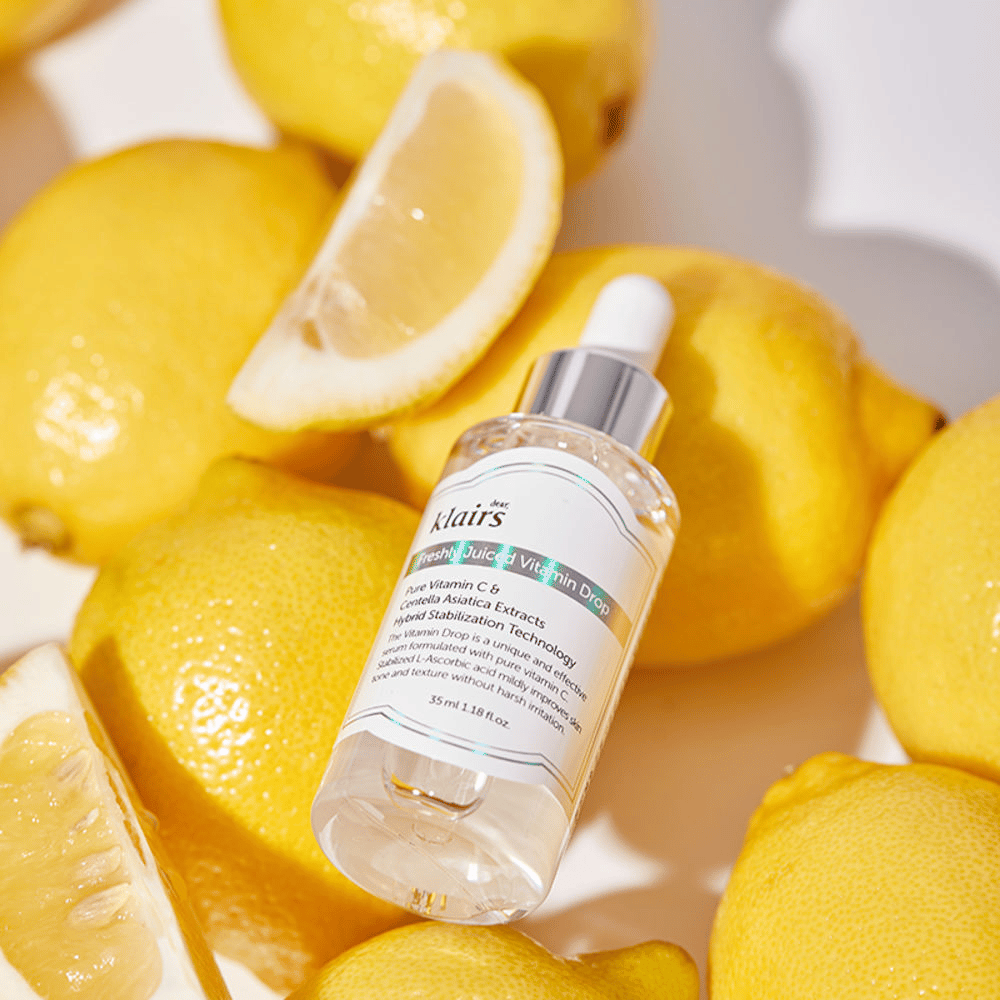 Klairs Freshly Juiced Vitamin Drop serum bottle surrounded by fresh lemon halves and lemon slices on a light surface, highlighting the ingredients.