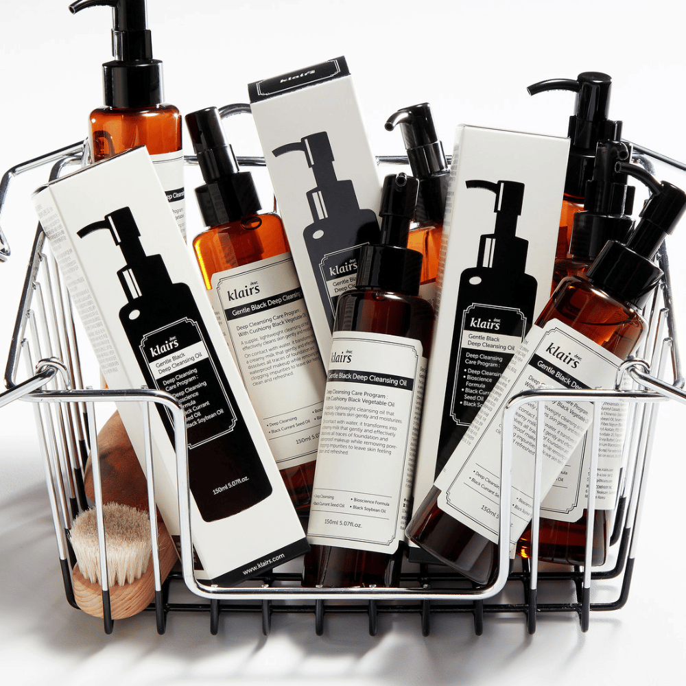 A mini shopping cart filled with skincare products from Klairs, including Gentle Black Deep Cleansing Oil in transparent bottles with black pumps and matching packaging.