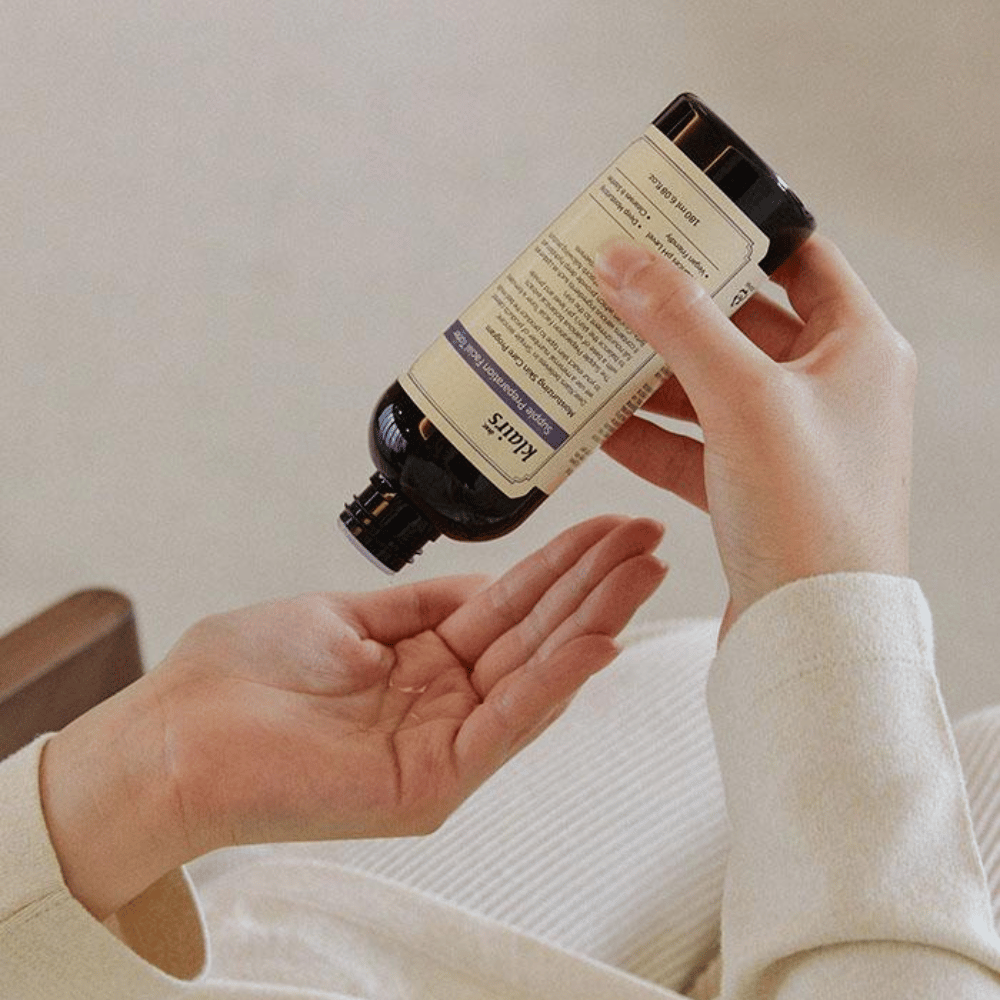 A person holds a bottle of Klairs Supple Preparation Facial Toner upside down over their hand, ready to dispense the product.