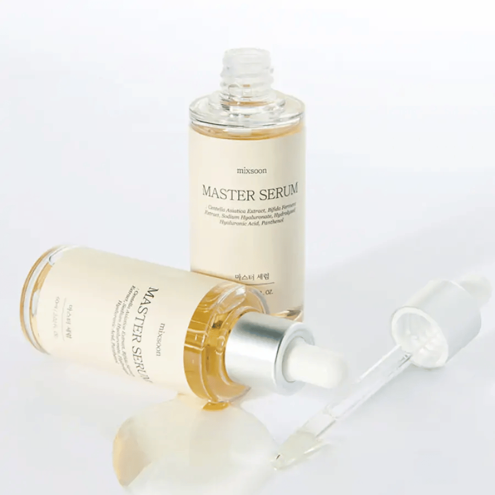 Two bottles of Mixsoon Master Serum, one standing and one lying with an open pipette, where the serum has spilled onto a white surface.