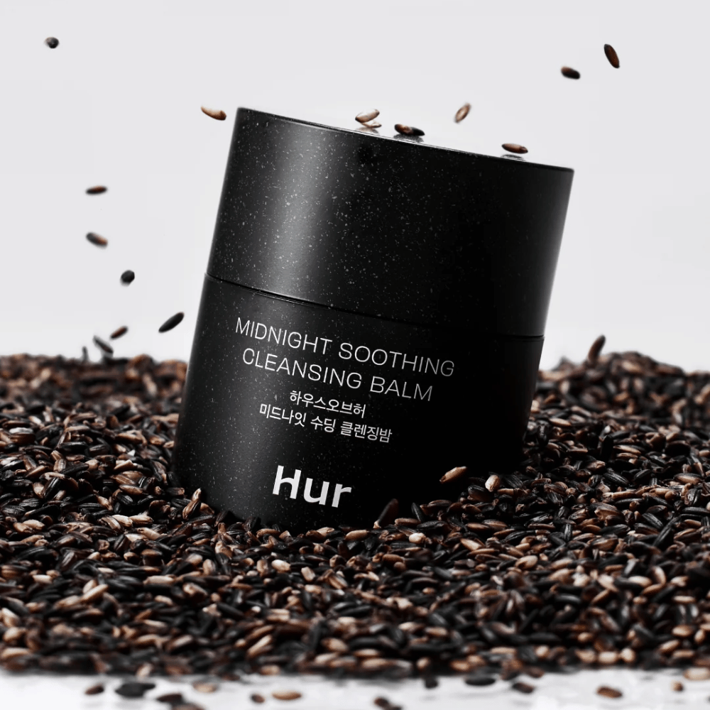 How Midnight Soothing Cleansing Balm in black jar placed on black seeds. Soothing cleansing balm that dissolves makeup and impurities while caring for the skin.