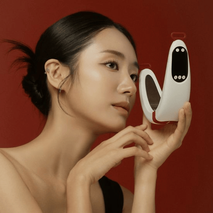 Model holding Beaund Nmode Pro in front of the face against a red background. The image highlights the device's elegant design, digital display, and compact format.