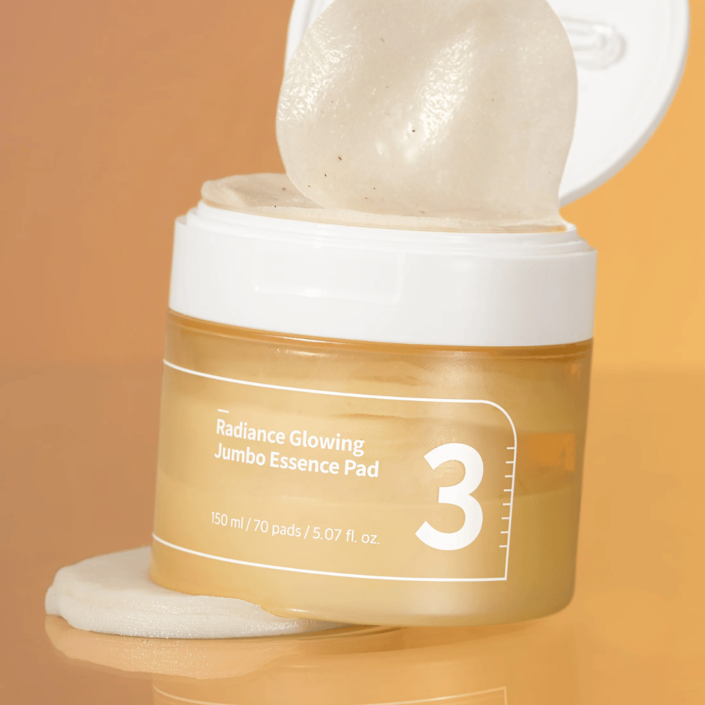Open jar with numbuzin No. 3 Radiance Glowing Jumbo Essence Pad, one pad is seen leaning against the edge, background in orange tone.
