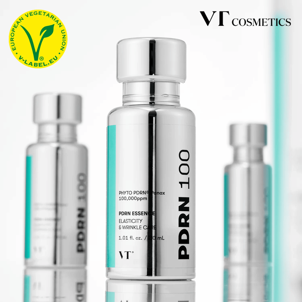 Several silver-colored bottles of VT PDRN 100 Essence are lined up, with clear labeling of 100,000 ppm PDRN and a focus on elasticity and wrinkle care. At the top, the logo of VT Cosmetics and a V-label for vegetarian content are visible.