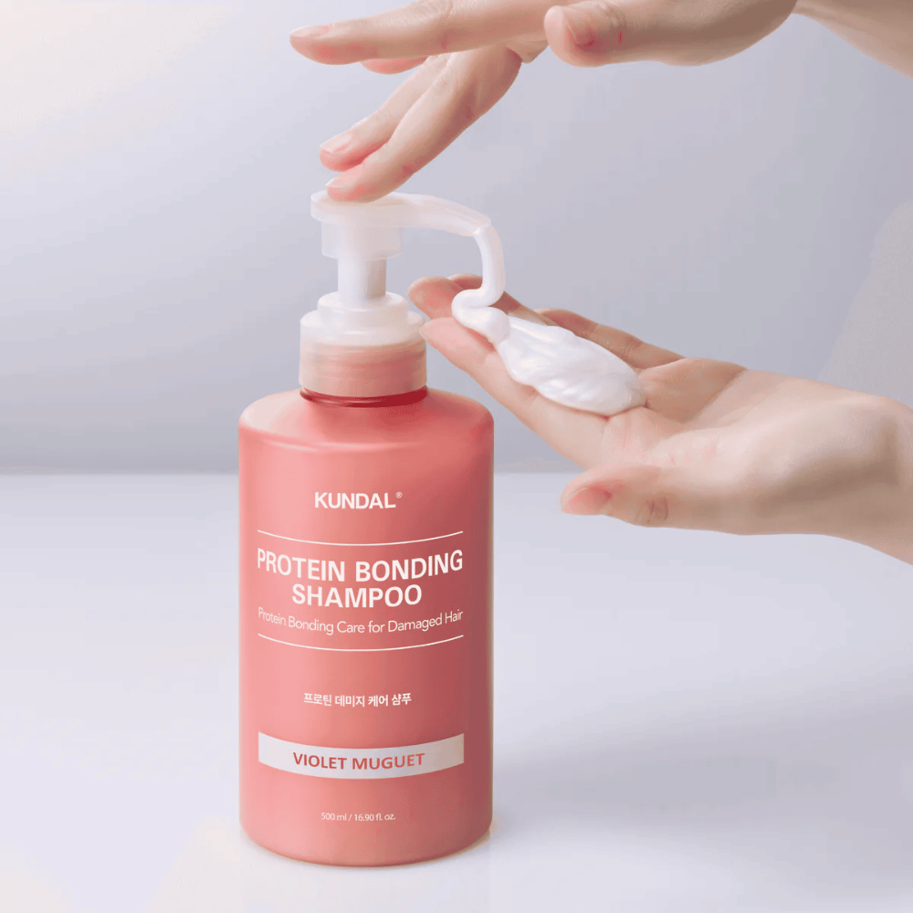 Hand pumps out KUNDAL Protein Bonding Shampoo Violet Muguet in creamy consistency, repairing shampoo for damaged hair.