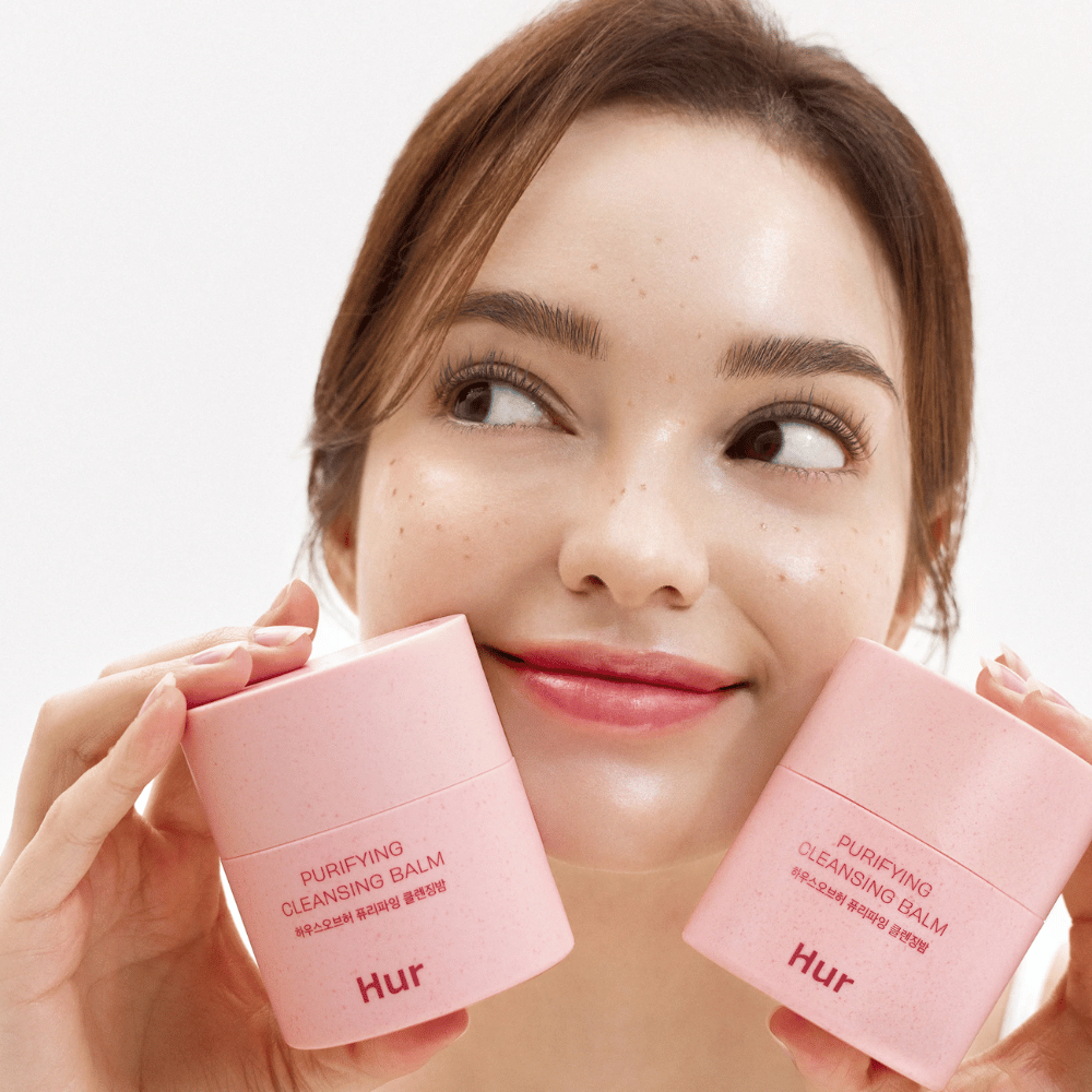 Model holding two jars of How Purifying Cleansing Balm. Mild cleansing balm suitable for sensitive skin and provides a fresh, hydrated feeling after cleansing.