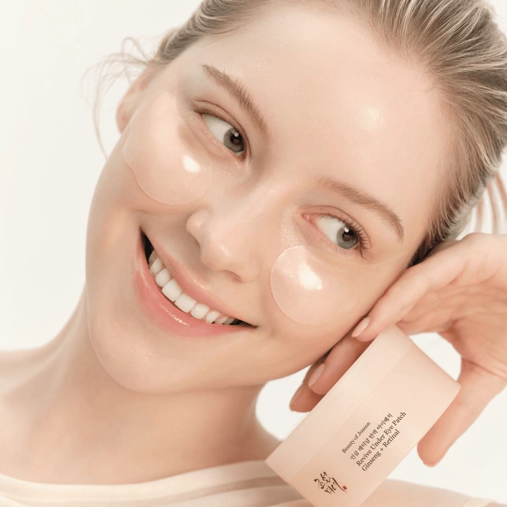 Model with Beauty of Joseon under eye patches and product in hand, eye patches with ginseng and retinal for a more awake and smoother eye area.