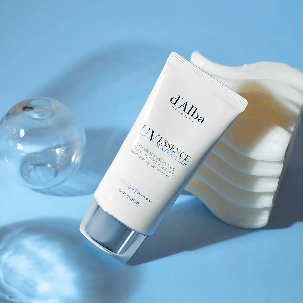 d'Alba UV Essence Waterfull+ Sun Cream med SPF 50+ PA++++ ligger mot en blå bakgrund med ljusreflektioner och dekorativa element – framhäver solkrämens fräscha och återfuktande egenskaper.