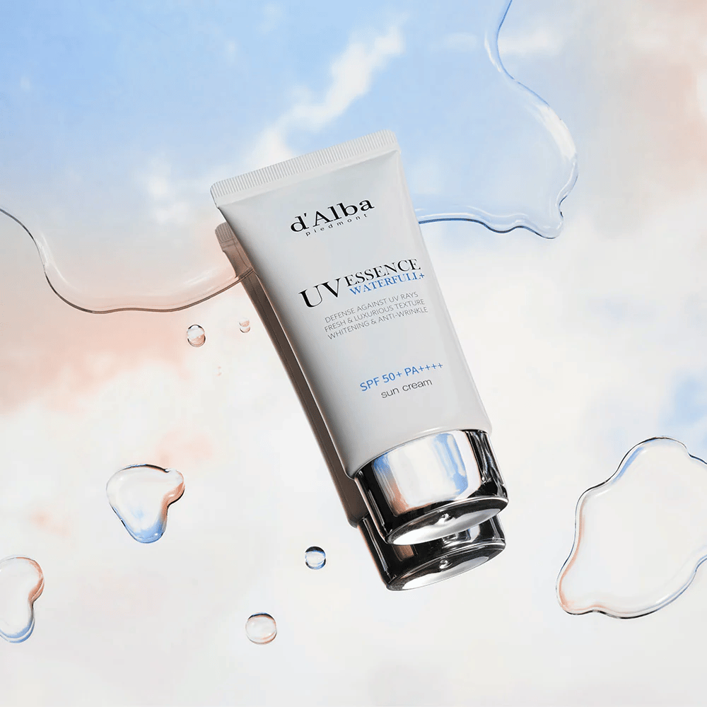Produktbild på d'Alba UV Essence Waterfull+ Sun Cream med SPF 50+ PA++++, placerad mot en bakgrund med vattenstänk och blårosa himmel – symboliserar lätt och återfuktande solskydd.