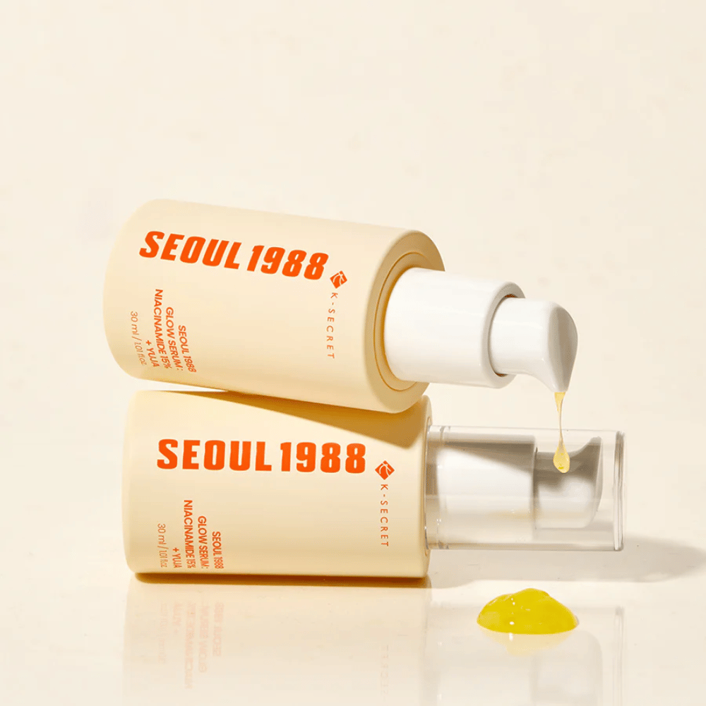 Two bottles of Seoul 1988 Glow Serum lying and standing, with yellow serum dripping from the pump.